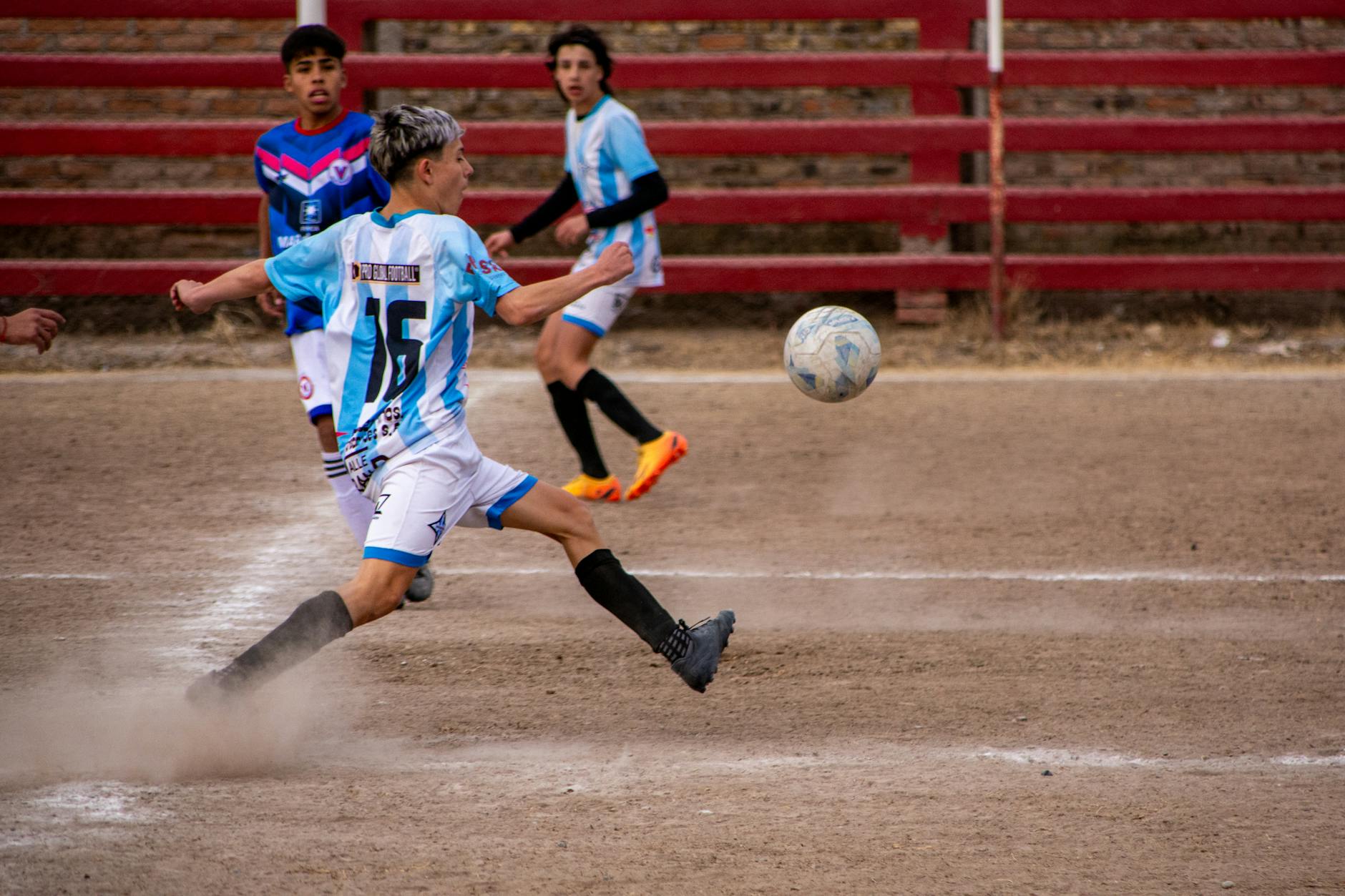 a group of boys playing soccer on a dirt field